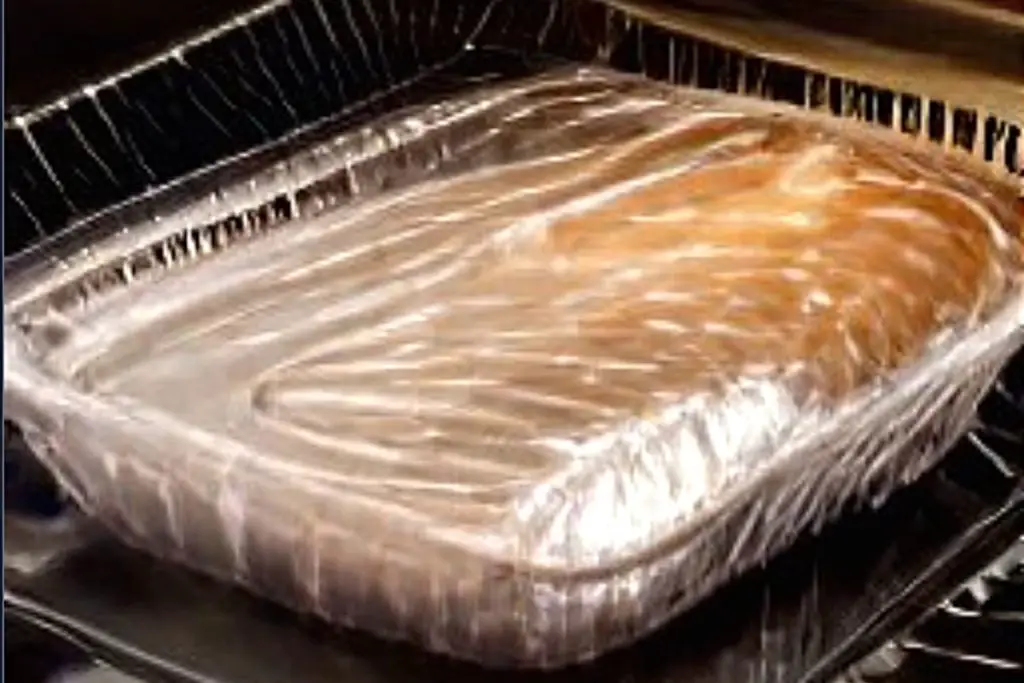 tray of food in the oven covered with plastic wrap