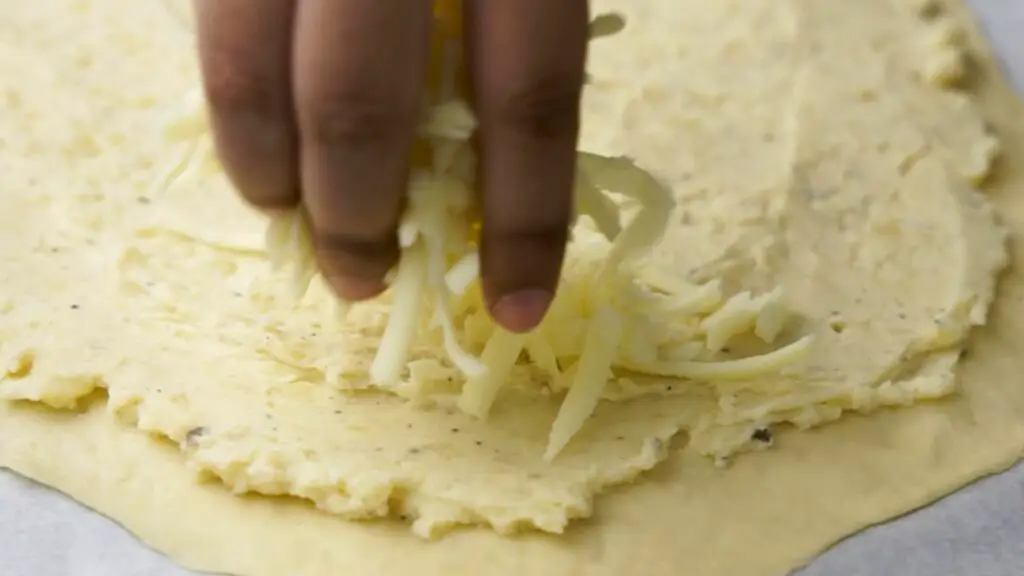 sprinkling the cheese on top of the potato filling