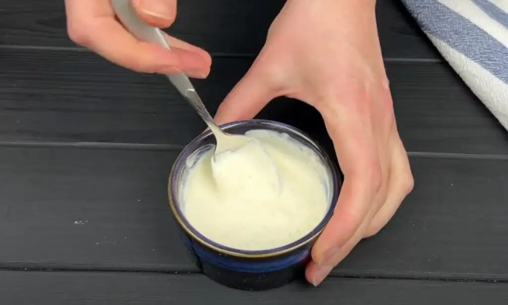 Hands stirring a creamy, homemade dip in a small blue ceramic bowl, perfect as an optional pairing for crispy Hasselback potatoes.