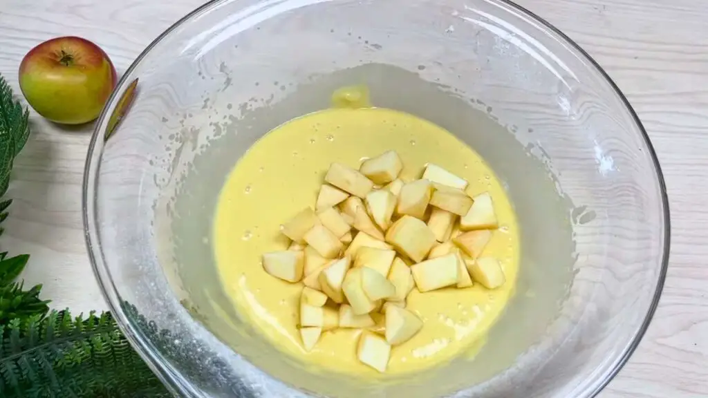 Chopped apples being added to a bowl of cake batter, showing a mixing step for an apple cinnamon loaf cake before baking.