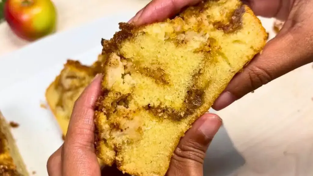 Close-up of hands holding a sliced loaf, showing the moist crumb, cinnamon swirls, and apple pieces that highlight the texture and flavor of apple cinnamon cake.