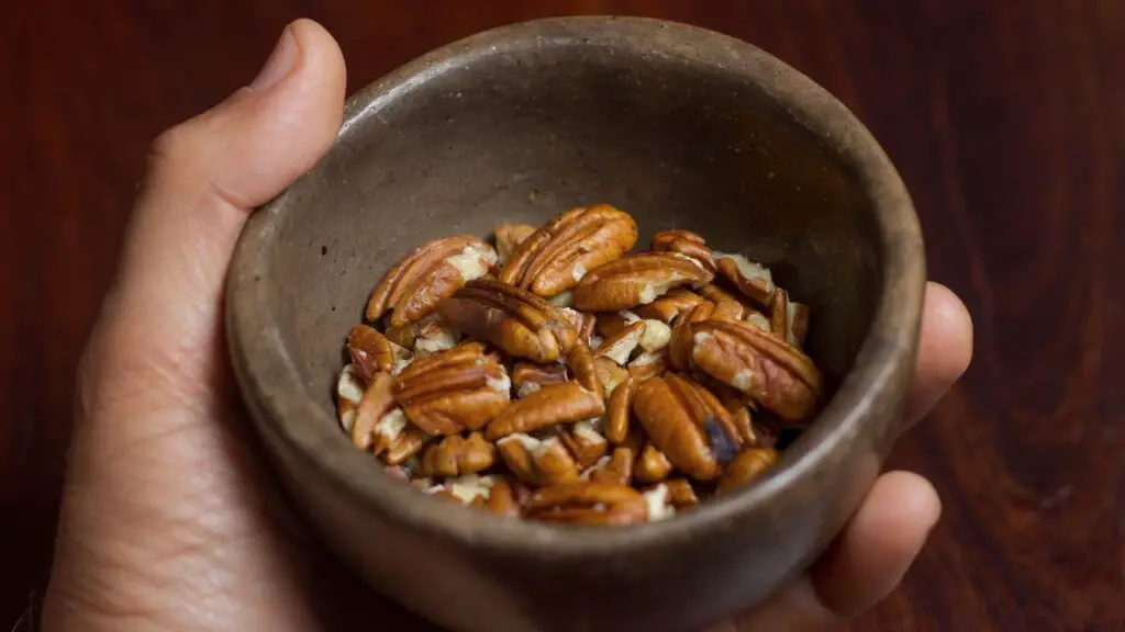 small bowl filled with chopped pecans, showing an easy nut swap option for baking, such as replacing walnuts in a healthy oat cake recipe