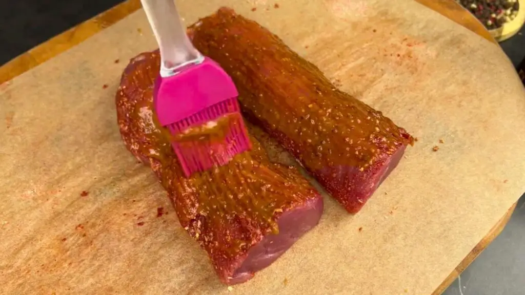 Barbecue sauce and Dijon mustard mixture brushed generously over pork tenderloin on parchment paper for air fryer pork tenderloin, coating the top evenly