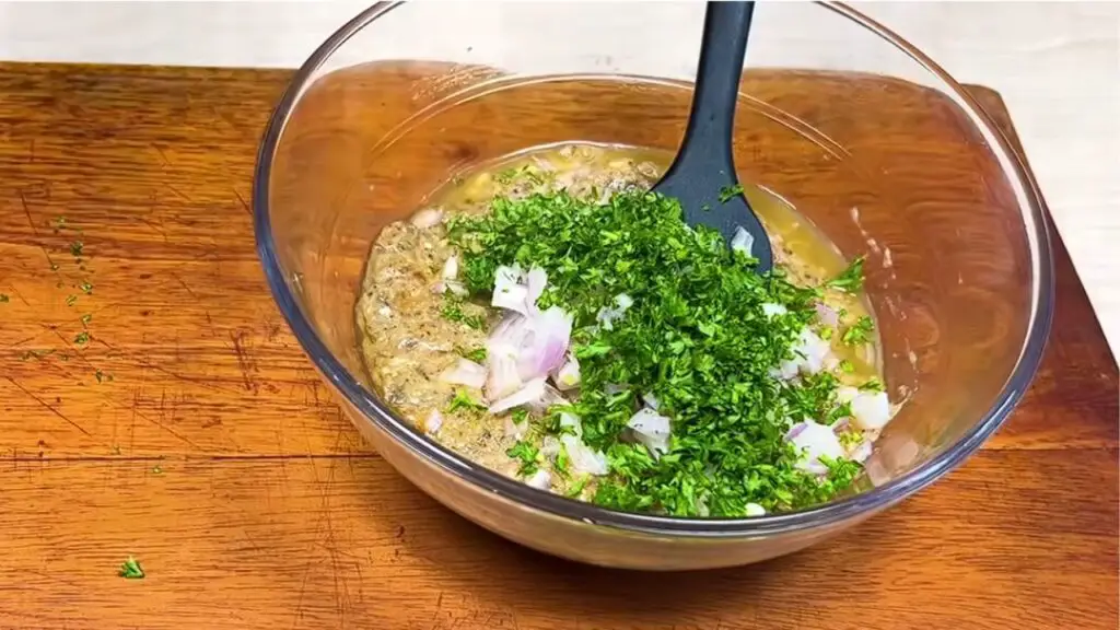 Chopped onion and fresh parsley are added to a bowl of sardine mixture, preparing sardine patties with canned sardines.