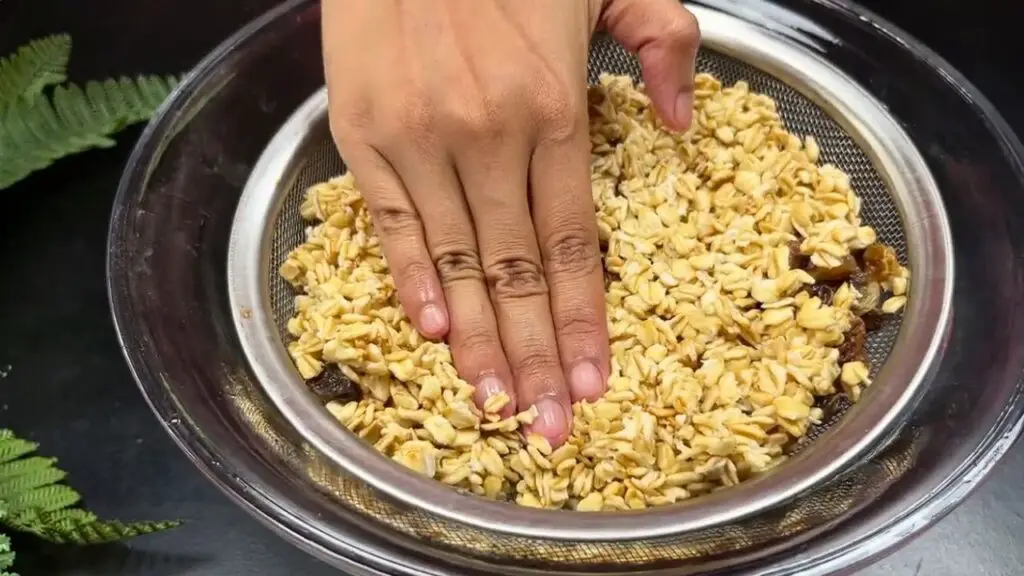 Draining soaked oats and raisins in a sieve, pressing out excess water for chewy banana oatmeal cookies.