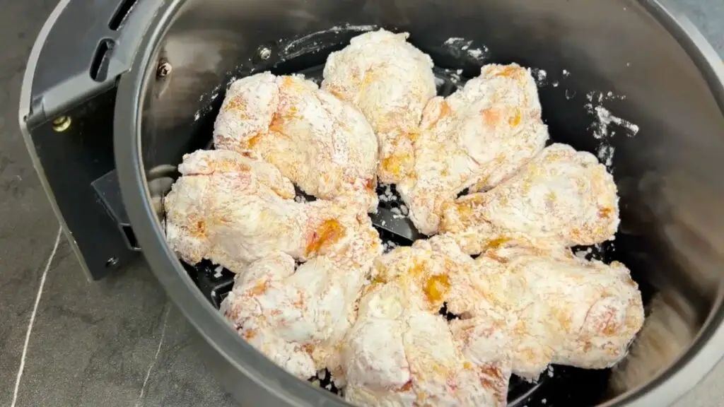 Flour-coated chicken wings arranged in a single layer inside an air fryer basket, ready to cook for crispy air fryer chicken wings.