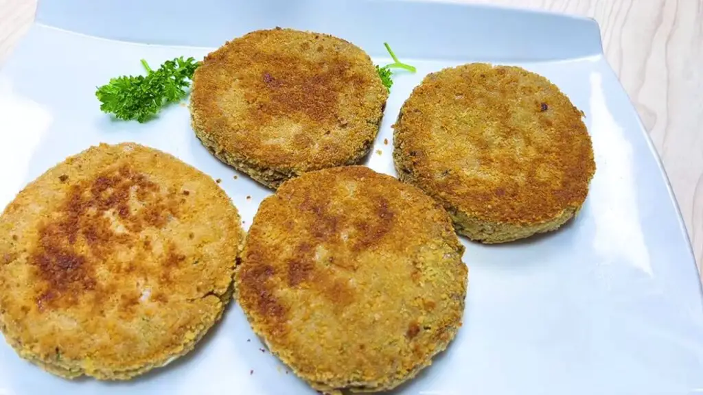Four golden patties served on a white plate with parsley garnish, showing cooked canned sardine fish cakes ready for storage or reheating.