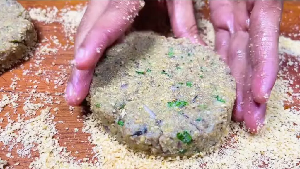 Hands shape a thick round patty from the fish mixture on a breadcrumb-covered surface, forming canned fish cakes.