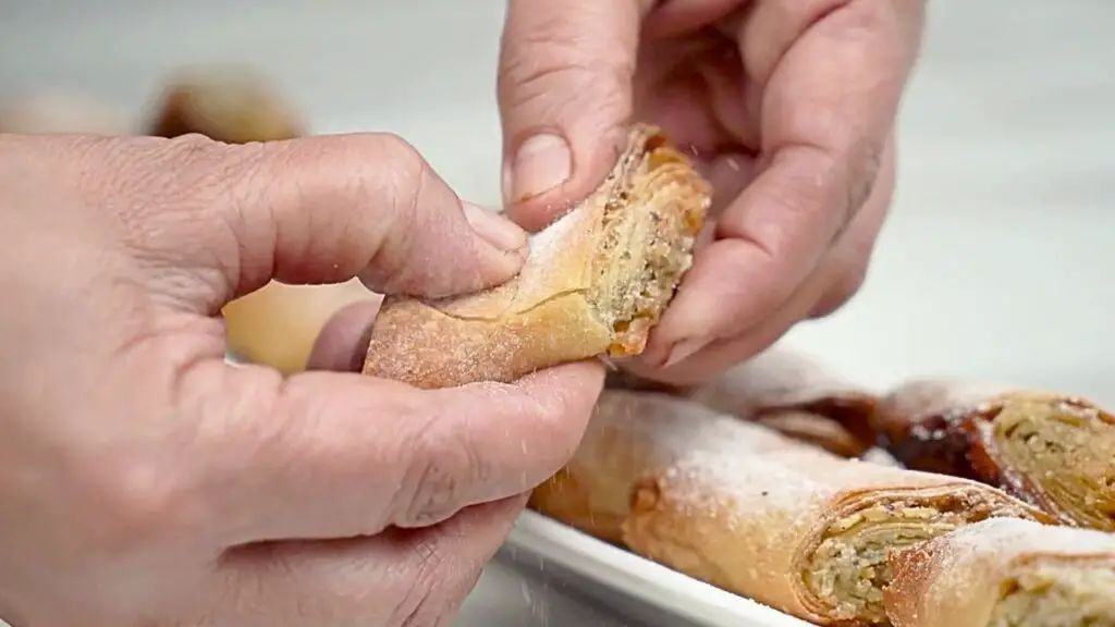 hands pulling apart crispy baklava to reveal golden, flaky phyllo layers and nut filling