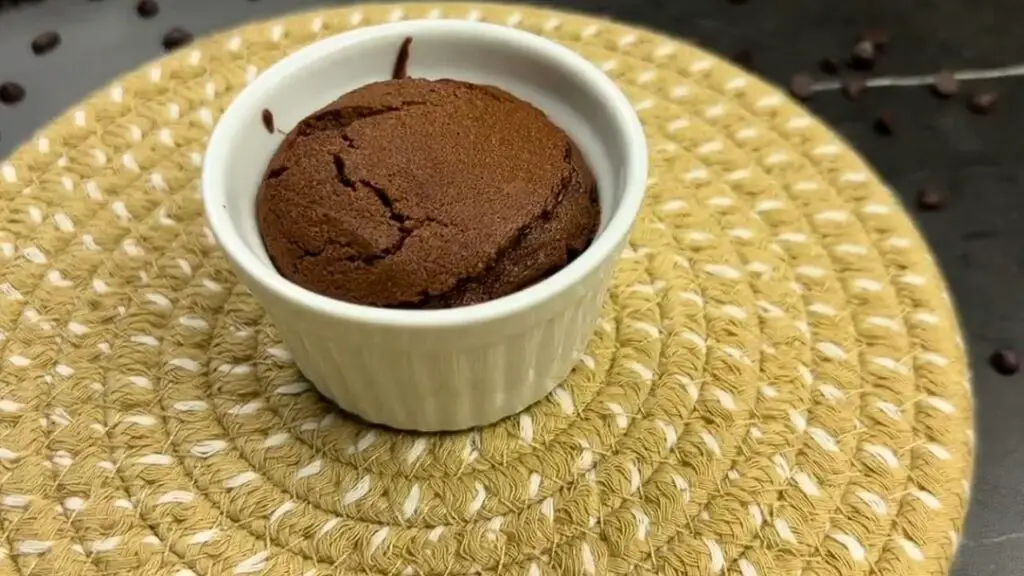 A baked chocolate brownie in a small white cup, slightly risen and cracked on top, ready to enjoy in a single serve brownie recipe.