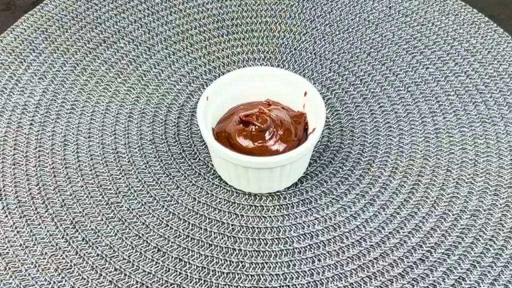 A small heat proof cup filled with chocolate brownie batter, leaving space at the top, ready to bake in an easy gooey brownie recipe.