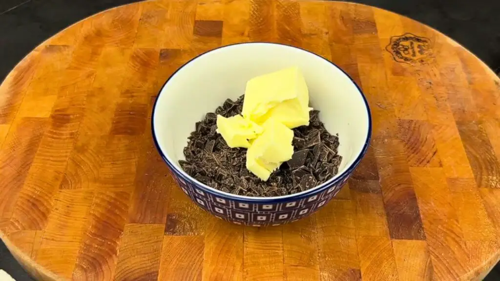 A small patterned bowl on a wooden cutting board filled with chopped chocolate and three pieces of butter, ready to be melted for an air fryer brownie recipe.
