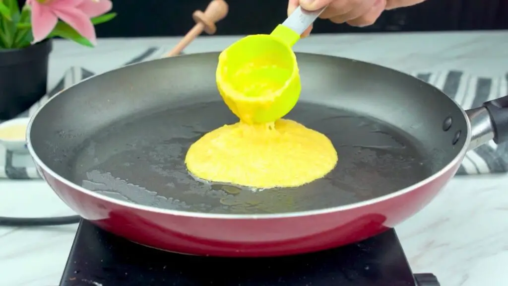 Batter being poured into a greased skillet to cook a gluten-free pancake on the stovetop.