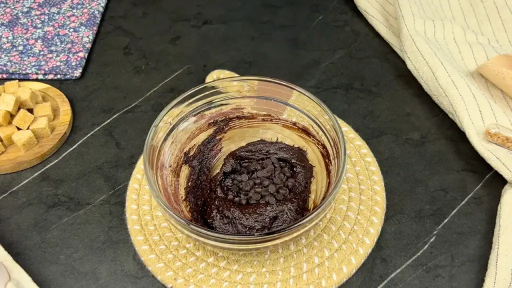 Chocolate batter in a glass bowl topped with chocolate chips for fudgy brownie cupcakes.