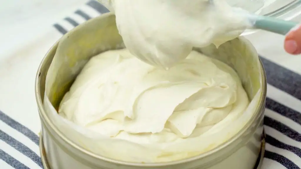 Creamy cheesecake filling being spread smoothly into a lined pan, part of a no bake cheesecake recipe.