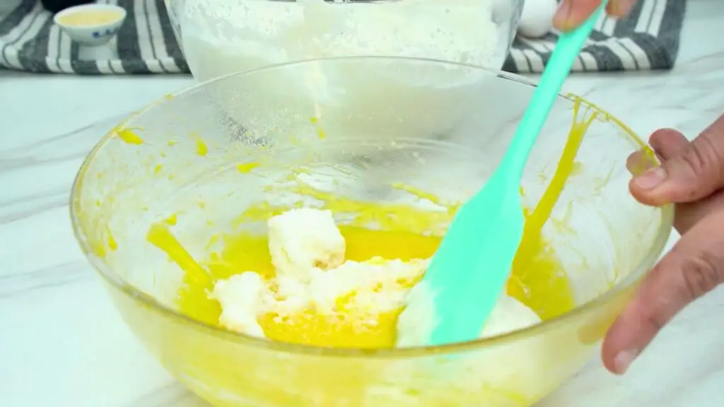 Egg whites being gently folded into egg yolk batter with a spatula while making protein pancakes.