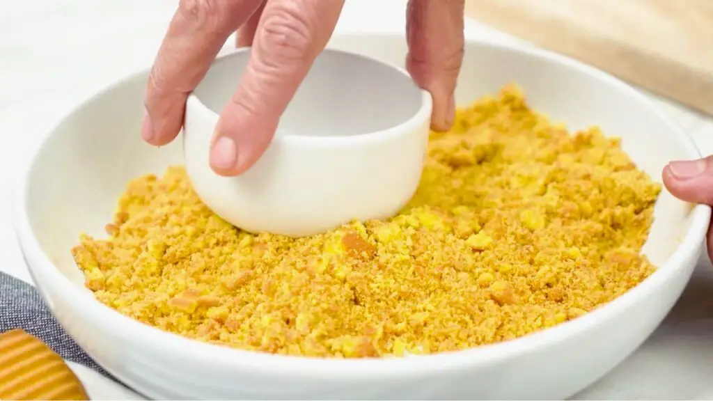 Fine cookie crumbs with a sandy texture pressed evenly into a dish using the back of a cup to form the crust base, one of the ingredients to make cheesecake.