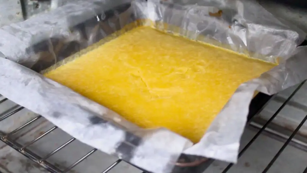 Freshly baked fudgy lemon brownies cooling in a parchment-lined 8x8 pan on an oven rack, showing the soft, set top after baking.