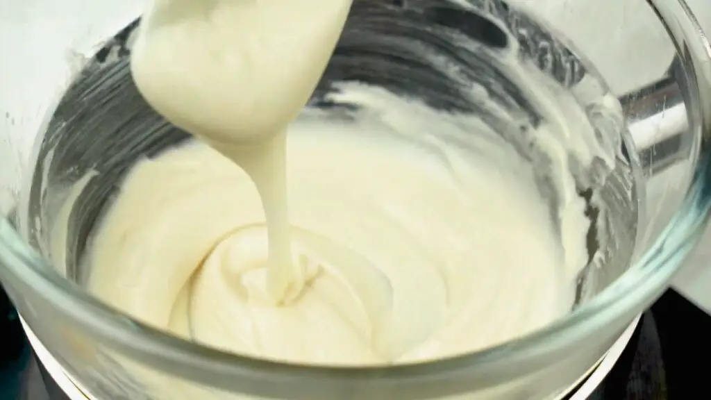 Melted white chocolate being stirred until glossy and smooth over gentle heat, a step in an easy cheesecake recipe.
