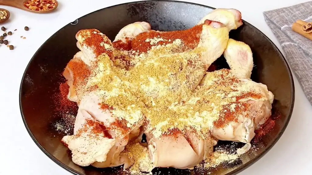 Raw chicken drumsticks in a bowl are generously coated with smoked paprika, ginger, garlic powder, onion powder, salt, black pepper, and curry powder, seasoned to make the best air fryer chicken drumsticks.