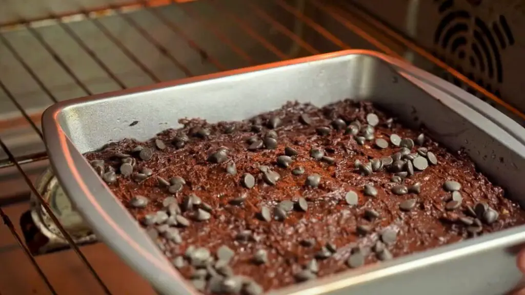 Square baking pan inside an oven filled with fudgy black bean brownies topped with chocolate chips