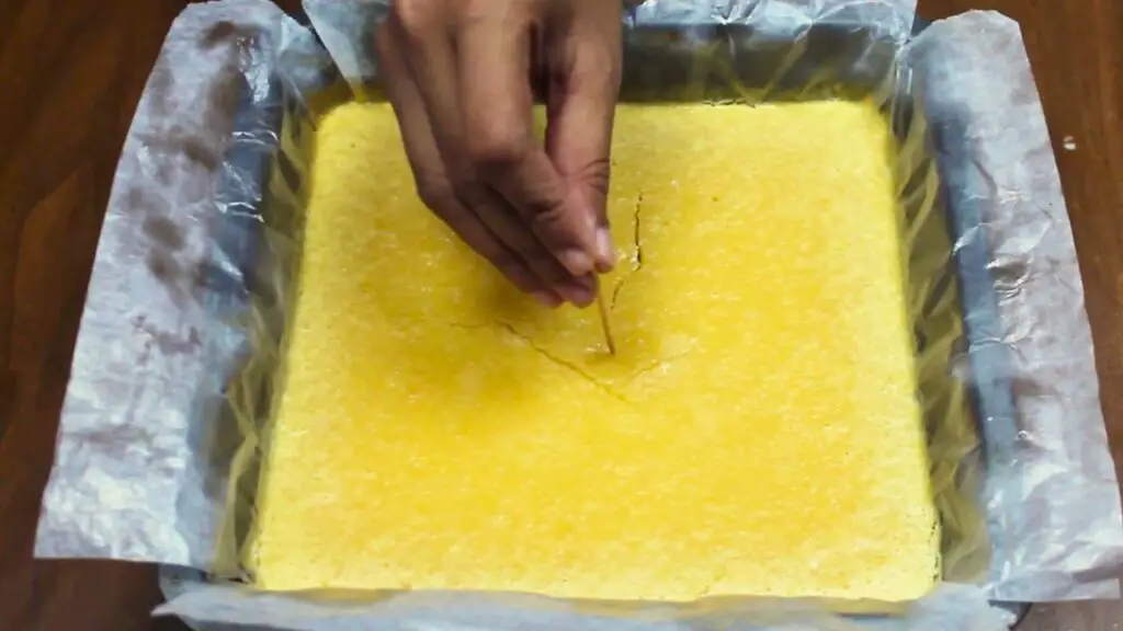 Toothpick testing doneness in freshly baked lemon brownies recipe in an 8x8 parchment-lined pan, checking that the center comes out clean.
