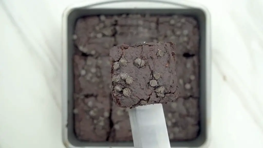 square piece of healthy brownies with chocolate chips held above a pan of cut brownies