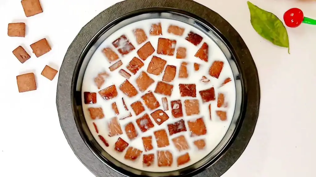 A bowl of healthy chocolate cereal is served with milk, showing crisp chocolate squares soaking and ready to eat.