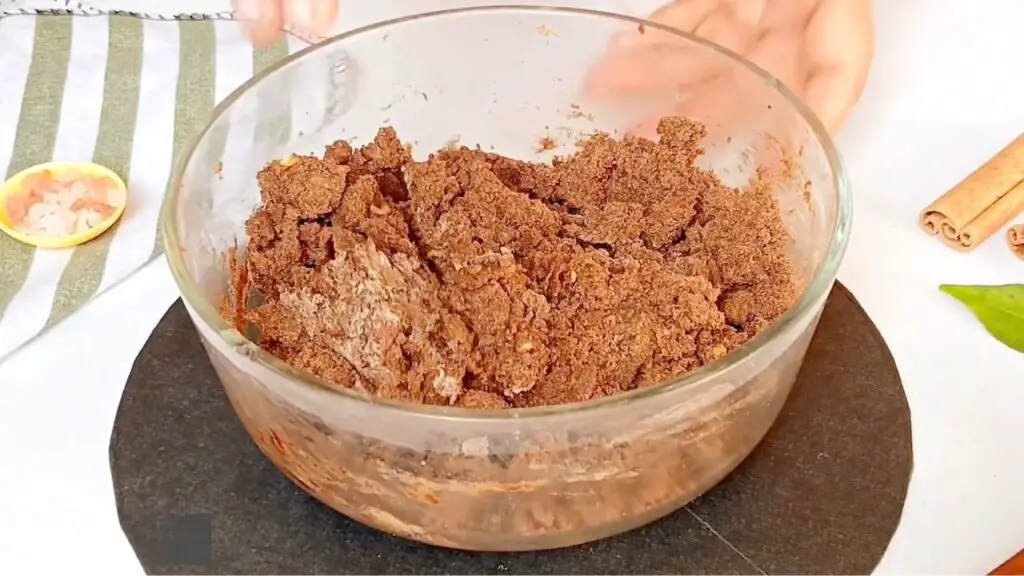 A crumbly chocolate oat mixture is being mixed in a bowl until evenly combined and able to hold together for homemade cereal with oats.