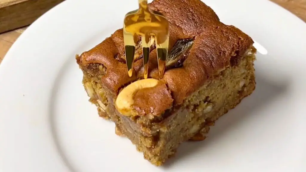 A moist slice of date cake topped with cashews and dates is drizzled with syrup on a plate in this grandmas cake recipe.
