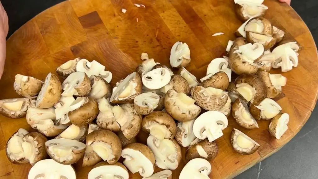 Air fryer garlic mushrooms- Fresh mushrooms sliced into quarters, with the stems trimmed, placed on a wooden cutting board ready for cooking.