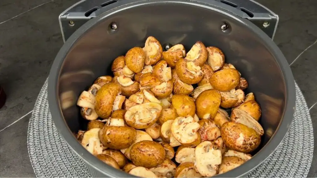 Air fryer mushrooms arranged in a fairly even layer inside the basket, ready to cook.