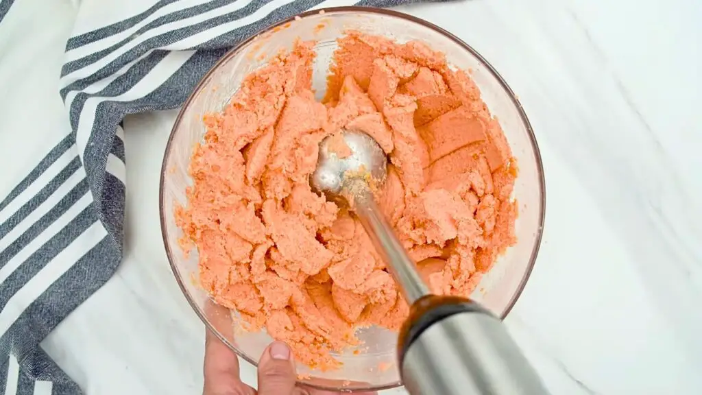 Blending soaked red lentils in a bowl with an immersion blender until smooth and creamy for a red lentil bread recipe.