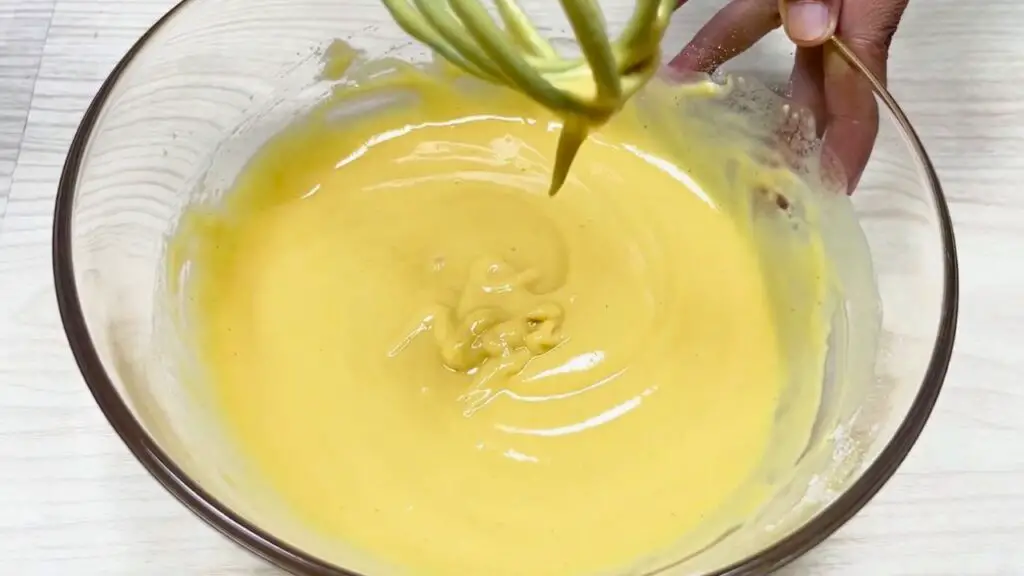 Chickpea Chips batter is being whisked in a glass bowl until smooth and pourable, with a light, lump-free consistency similar to thin pancake batter.
