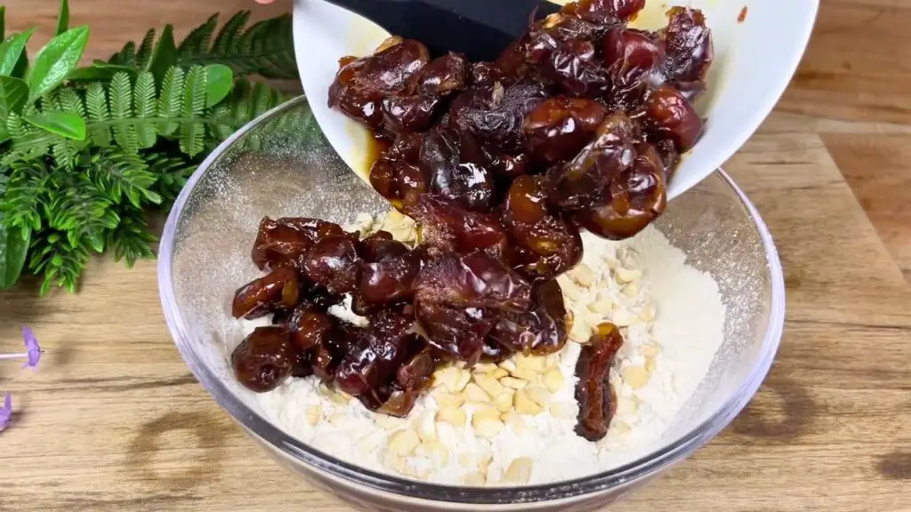 Chopped soaked dates are added to a bowl of flour and chopped cashews and gently mixed for even distribution in this easy date cake recipe.