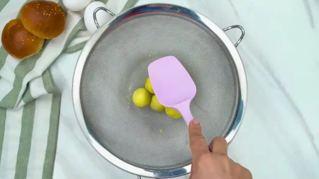 Egg yolks being pressed through a fine mesh sieve with a spoon to create a soft, fluffy texture for a unique egg salad recipe