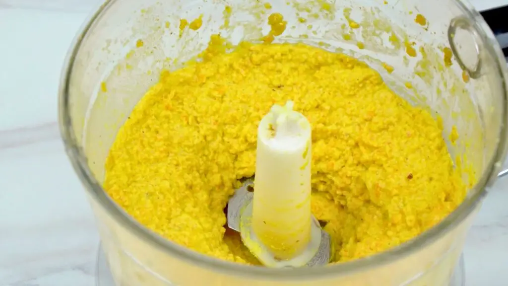 Food processor blending a thick yellow lentil mixture into a smooth paste, prepared as the batter for crispy lentil crackers.