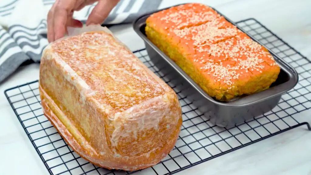 Freshly baked red lentil gluten free bread cooling on a wire rack as parchment paper is peeled away from the loaf.