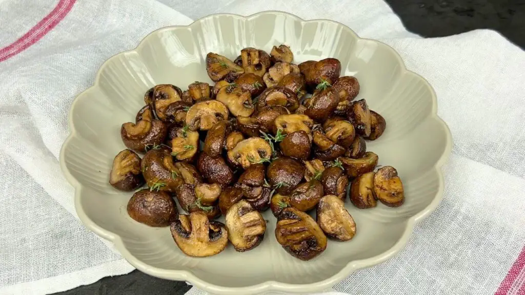 Perfectly cooked air fryer mushrooms garnished with fresh parsley, arranged neatly in a light-coloured bowl on a cloth napkin.