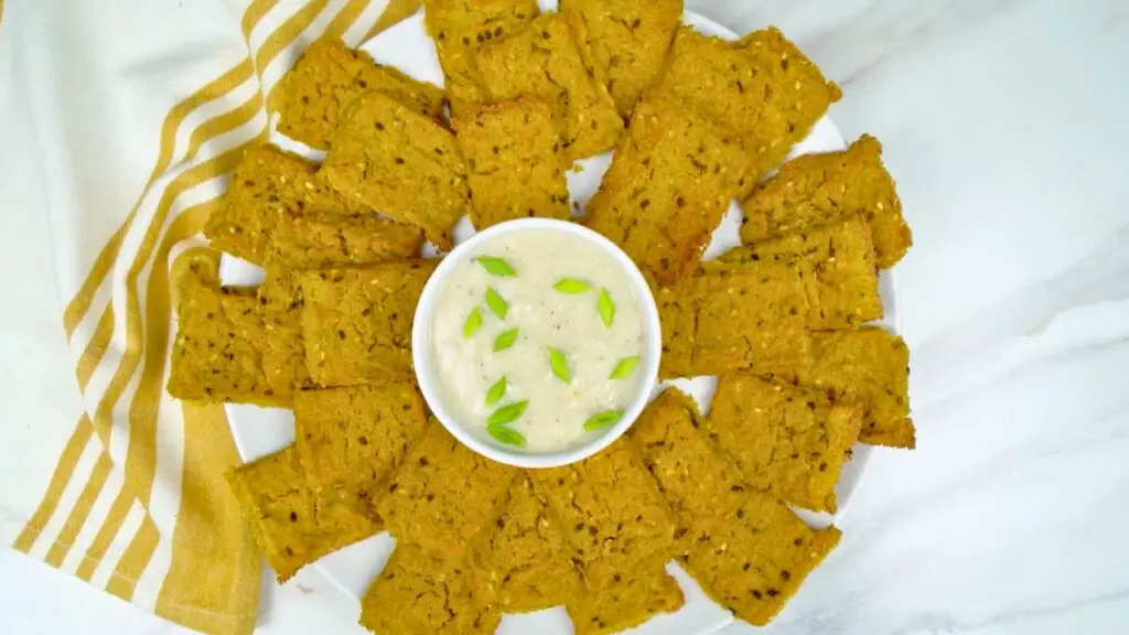 Plate of golden homemade crackers arranged around a small bowl of creamy dip topped with green onions, served in this baked crackers recipe.