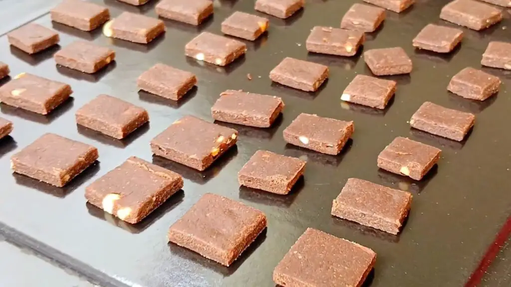 Small chocolate cereal squares are arranged on a baking sheet, ready to bake until crisp and golden for a crunchy oat cereal recipe.