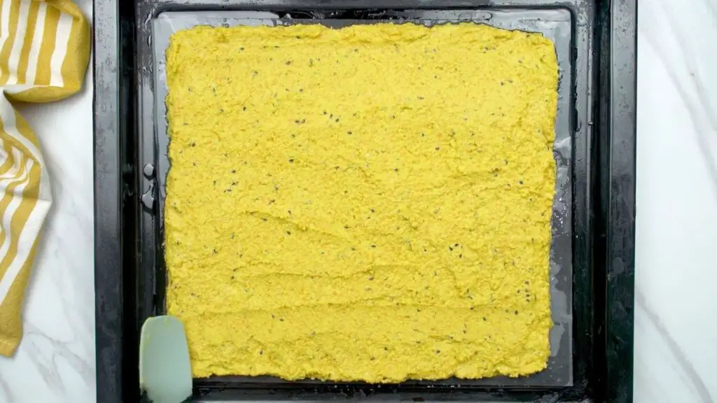 Thin layer of lentil batter spread evenly on a parchment-lined baking sheet, ready to bake in this healthy crackers recipe.