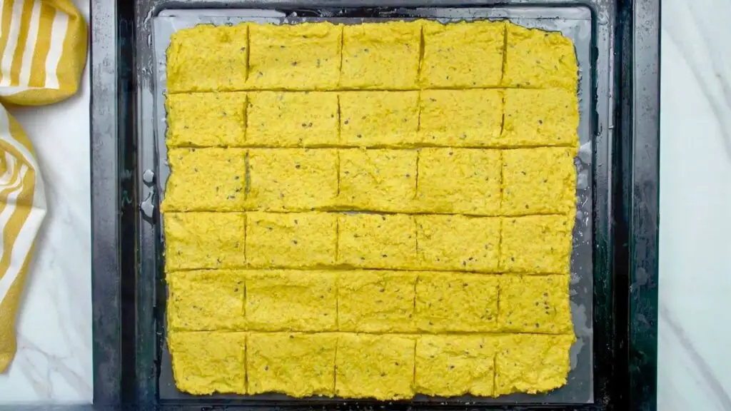 Thin layer of lentil batter spread on a parchment-lined baking sheet and scored into rectangles, prepared for baking in this lentil crackers recipe.