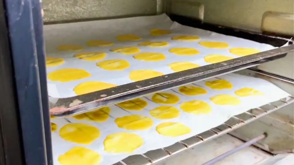 Thin rounds of batter are baking on parchment-lined trays in the oven, turning lightly golden and crisp for best homemade oven chips.