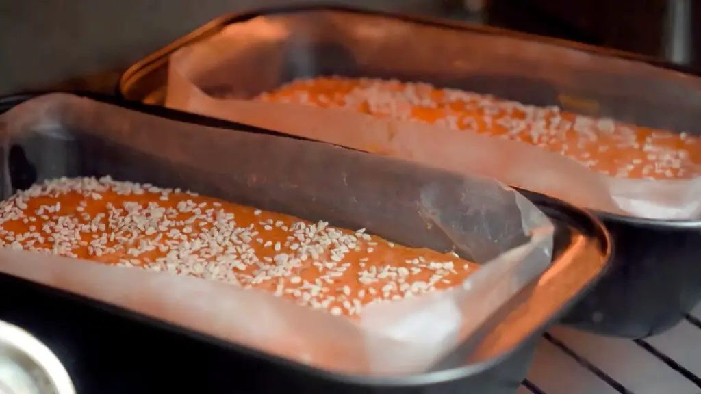 Two parchment-lined loaf pans with sesame-topped red lentil batter baking in the oven for a simple red lentil bread recipe.