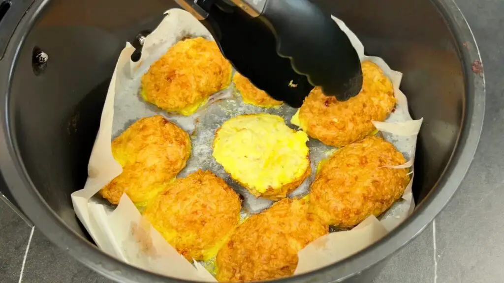 Air fryer chicken nuggets being reheated in a basket with tongs, showing crispy texture for easy storage and reheating method.