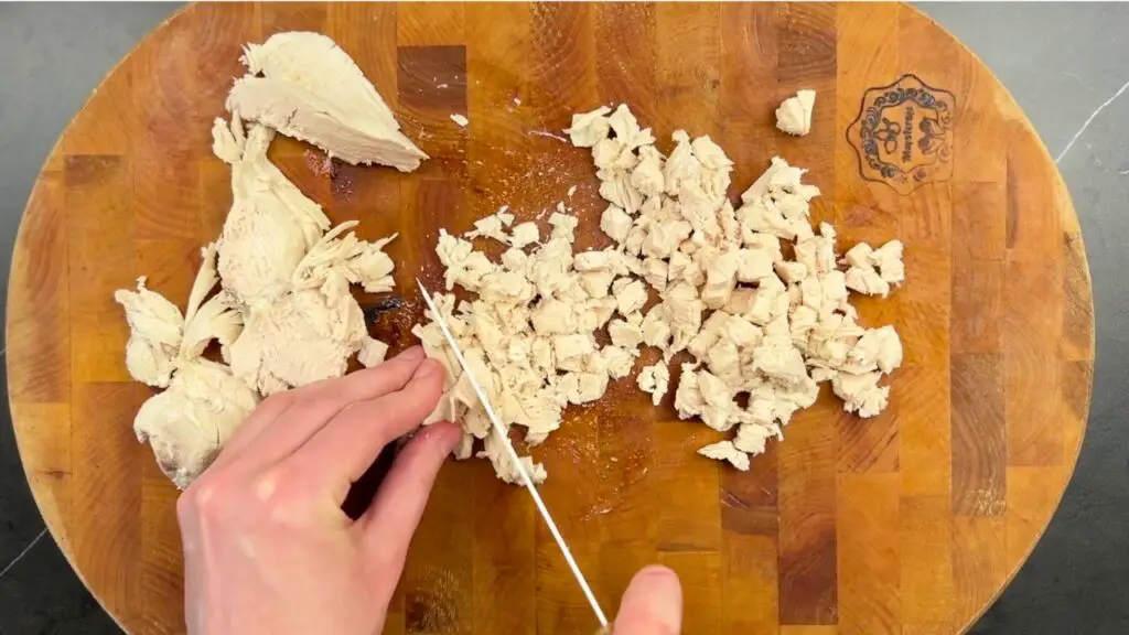 Air fryer chicken nuggets step showing hands finely chopping cooked chicken into small pieces on a wooden cutting board with a knife.