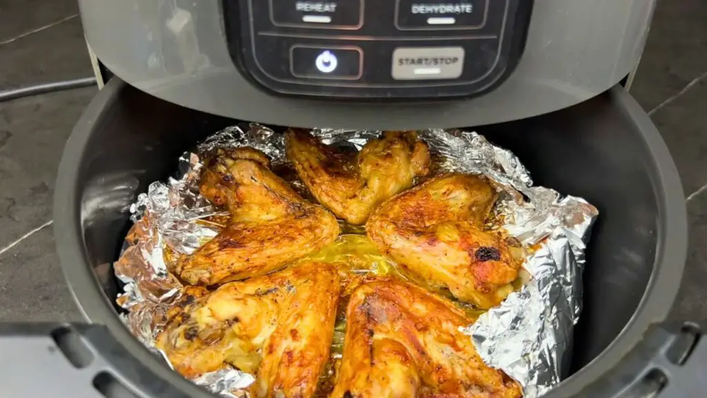 Air fryer chicken wings cooking on foil in basket at 400°F until crispy and golden brown.