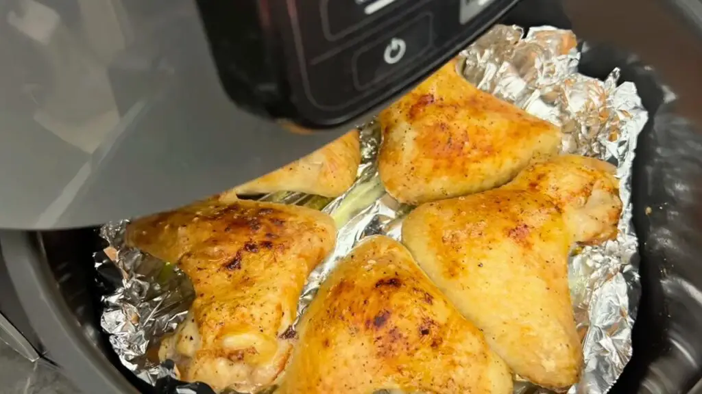 Air fryer chicken wings reheating in basket on foil, showing crispy golden skin