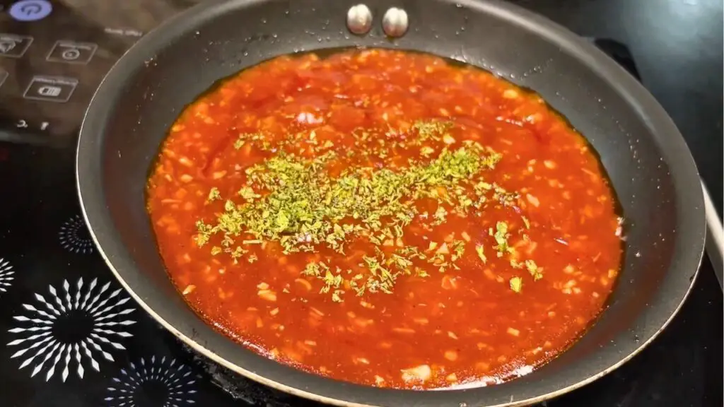 Best canned sardine recipe step showing tomato sauce simmering in a pan with dried parsley added and stirred until slightly thickened.
